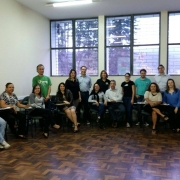 Sala de aula com ampla janela ao fundo e pessoas sentadas em meio círculo.