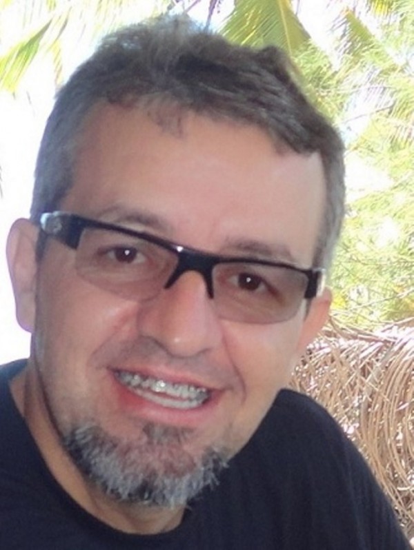 Homem sorridente de pele clara, cabelo e cavanhaque grisalhos. Usa óculos de grau pretos.