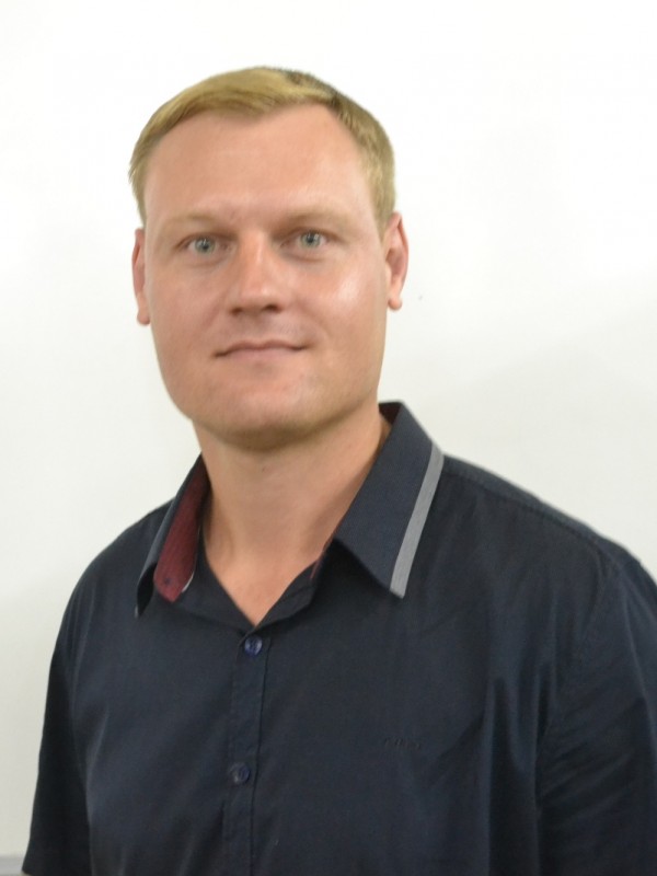 Homem de pele clara, olhos azuis e cabelos louros e curtos.