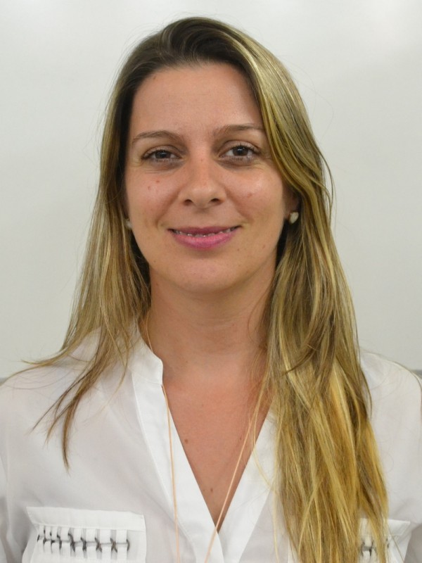 Mulher sorridente de pele cara, cabelo ondulado, louro e comprido. Veste camisa branca.