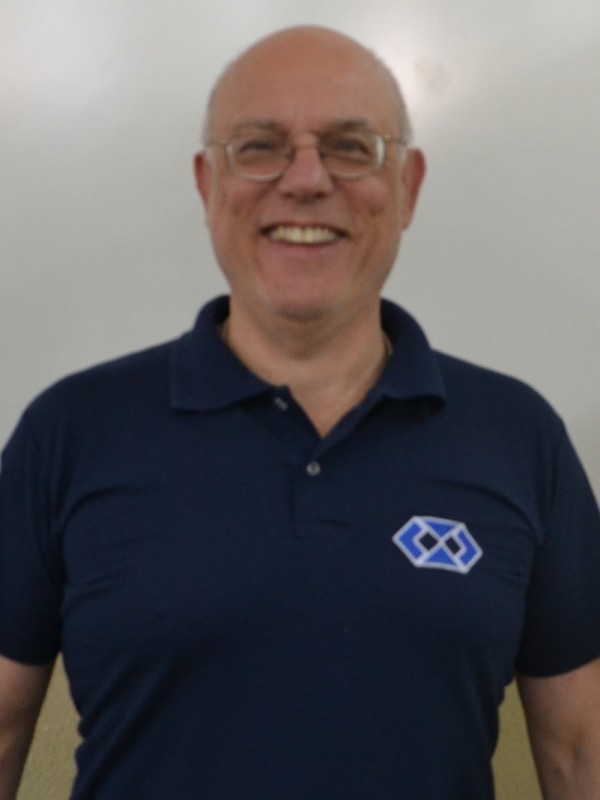 Homem sorridente de pele clara e calvo. Usa óculos de grau e veste camisa polo azul marinho.