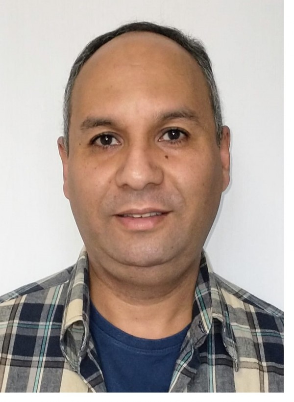 Homem de pele morena, cabelos grisalhos, levemente calvo.