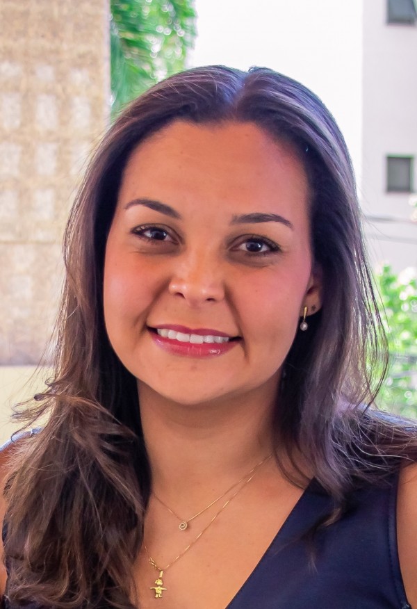 Mulher sorridente de pele morena, cabelos castanhos, lisos e compridos.