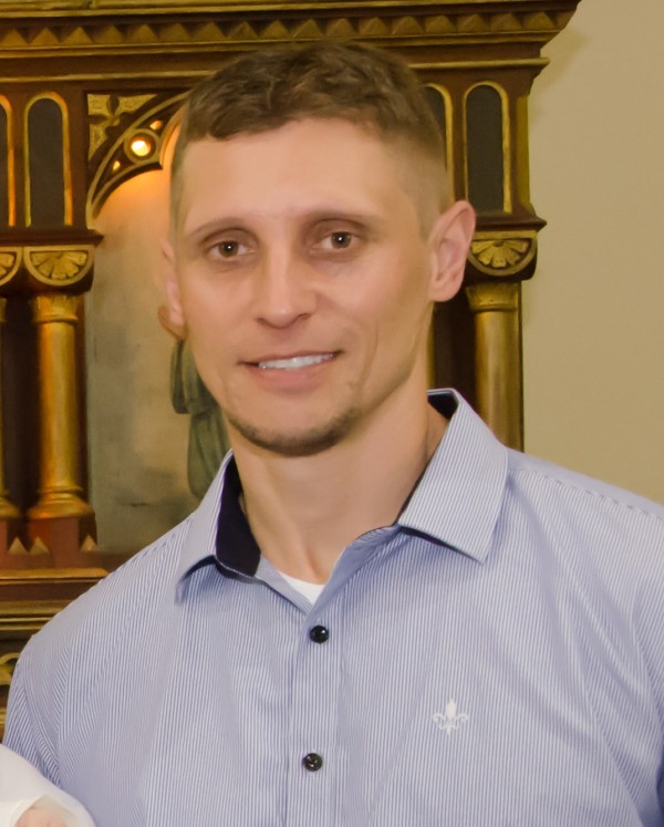 Homem sorridente de pele clara, cabelo curto louro e cavanhaque. Veste camisa azul.