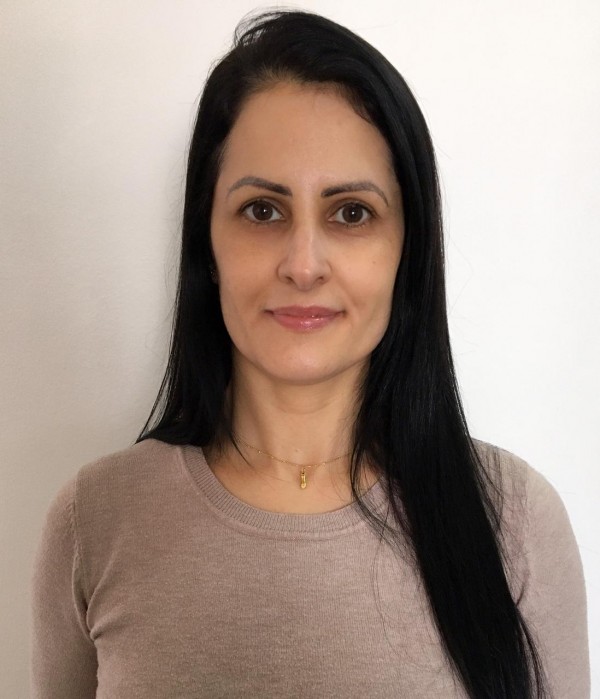 Mulher de pele morena cara, olhos castanhos, cabelo preto, liso e comprido. Veste blusa bege.