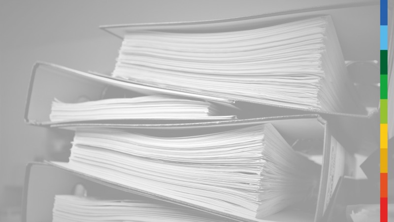 Imagem em preto e branco de quatro arquivos de papel empilhados. Na lateral direita da imagem, uma faixa colorida vertical.