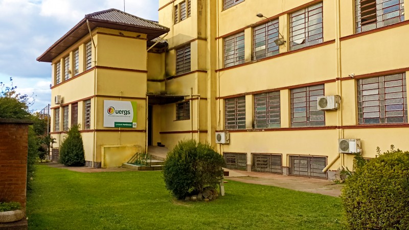 Foto do pr&eacute;dio da Unidade, com mais de 4 andares e paredes em tons de amarelo. Na parede do canto esquerdo, a placa de identifica&ccedil;&atilde;o da Uergs.