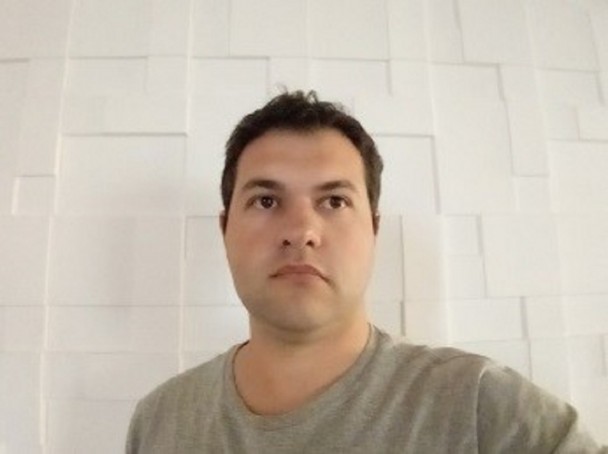 Homem de pele morena clara, olhos e cabelos curtos escuros.