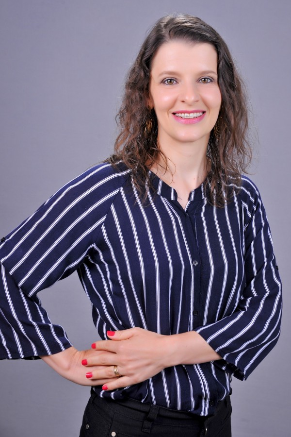 Mulher sorridente de pele morena clara, olhos castanhos e cabelos castanhos claro ondulados.