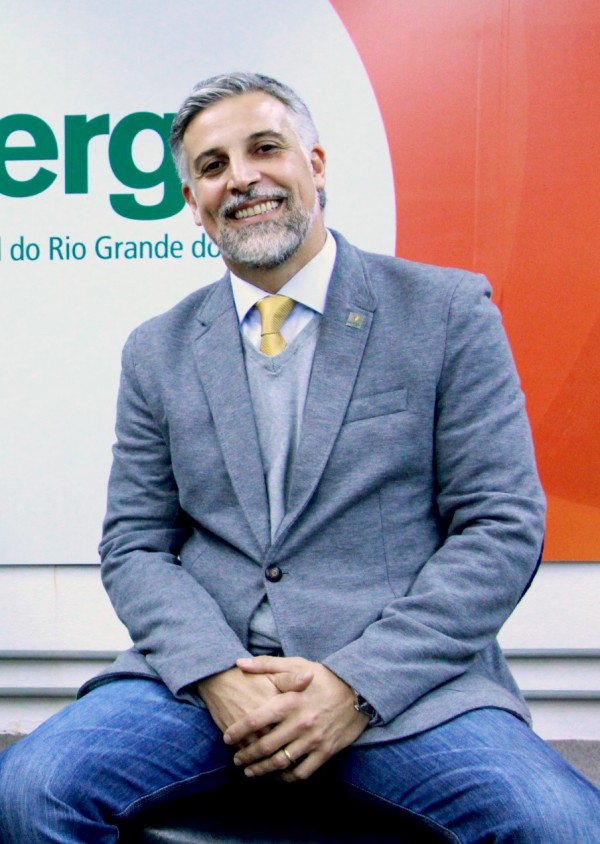 Homem sorridente de pele clara e cabelos grisalhos e curtos. Veste blazer cinza.